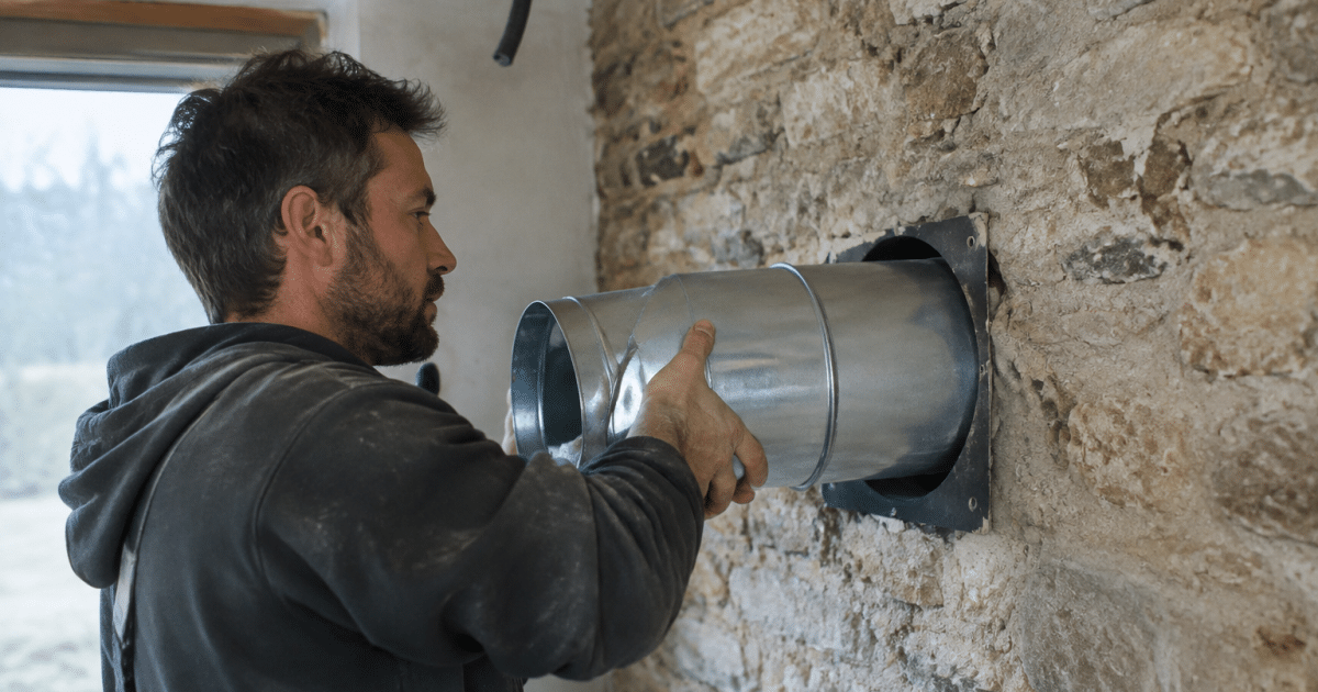 Technicien installant conduit ventilation traversant mur pierre ancienne