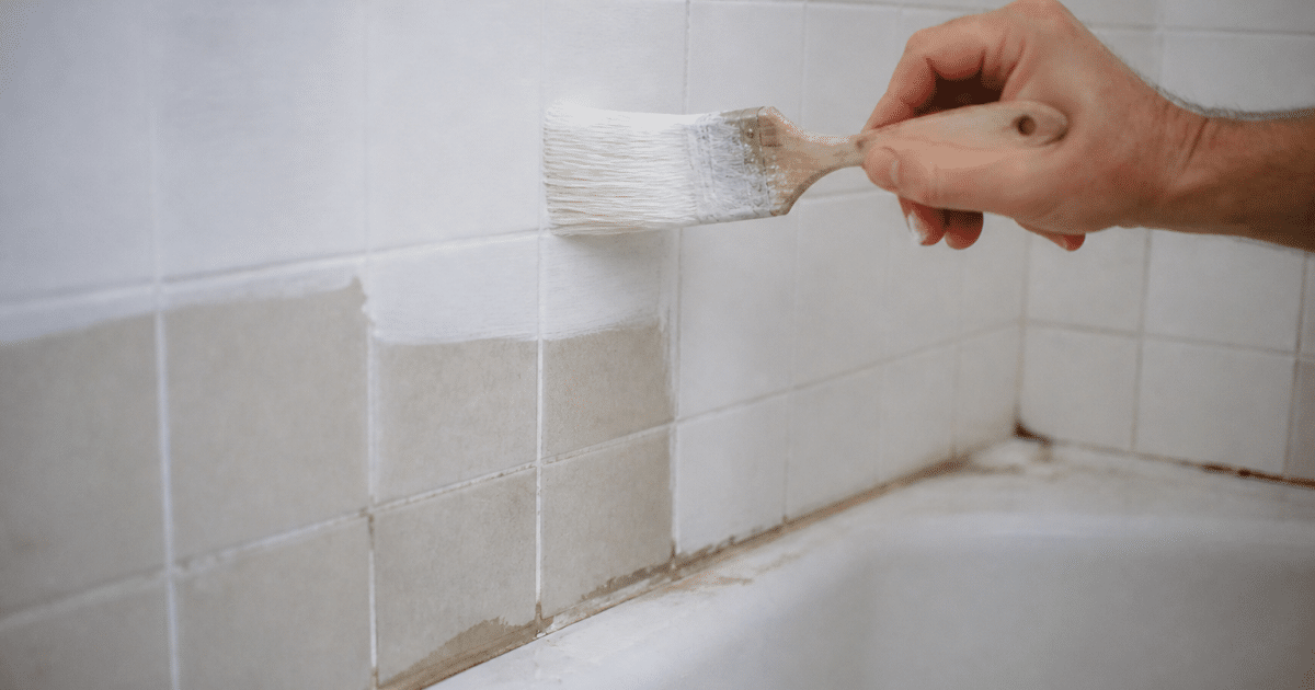 Pinceau appliquant peinture blanche sur carrelage mural salle bain