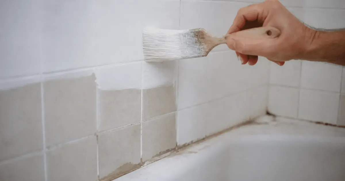 Pinceau appliquant peinture blanche sur carrelage mural salle bain