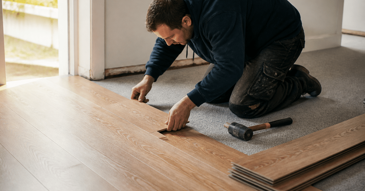 Ouvrier posant planches bois sur moquette grise existante