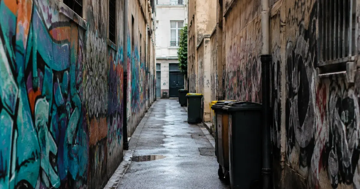 Rue étroite vide bordée de murs graffités et poubelles